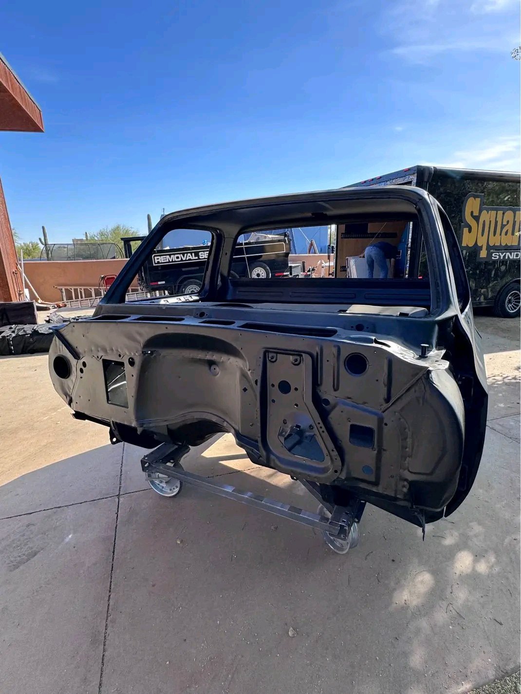 truck cab shell, resembling a 1973–1987 Chevrolet or GMC “squarebody” pickup truck cab mounted on a rolling dolly. [1]